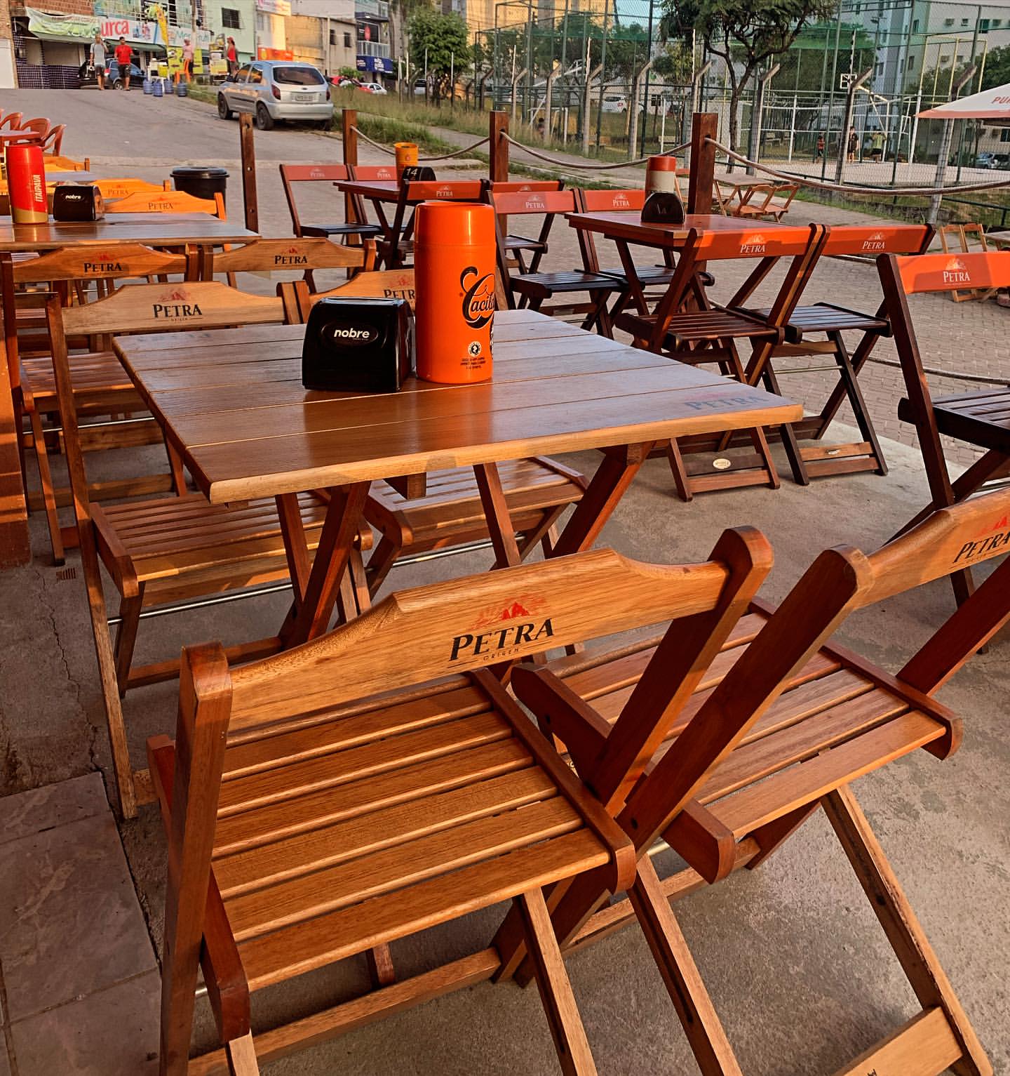 Mesas e cadeiras de madeira na área externa do Petrocerva Gastrobar